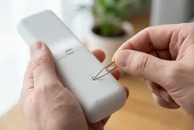 Gros plan sur l'utilisation d'un trombone pour réinitialiser une télécommande de climatisation