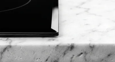 Gros plan sur l'épaisseur et la finition d'une plaque induction sur un plan de travail en marbre.